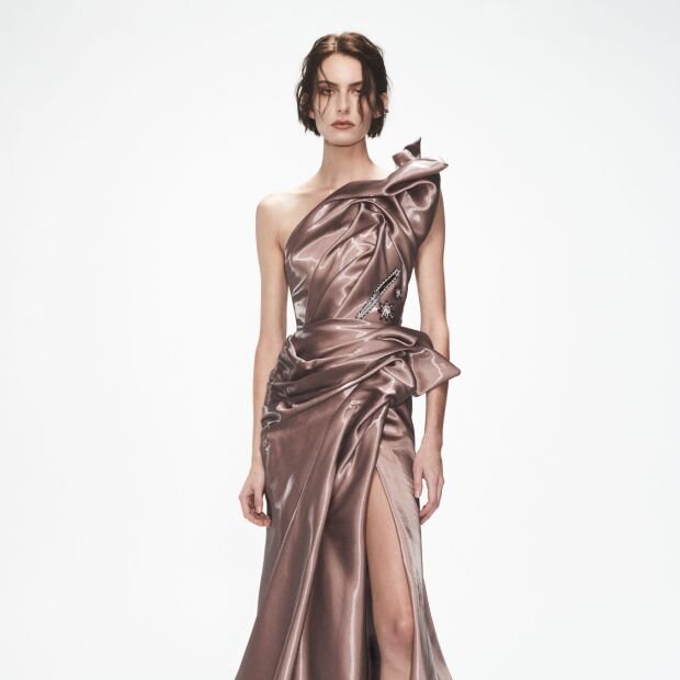A model wearing a rose gold gown with a glossy finish and structural details.