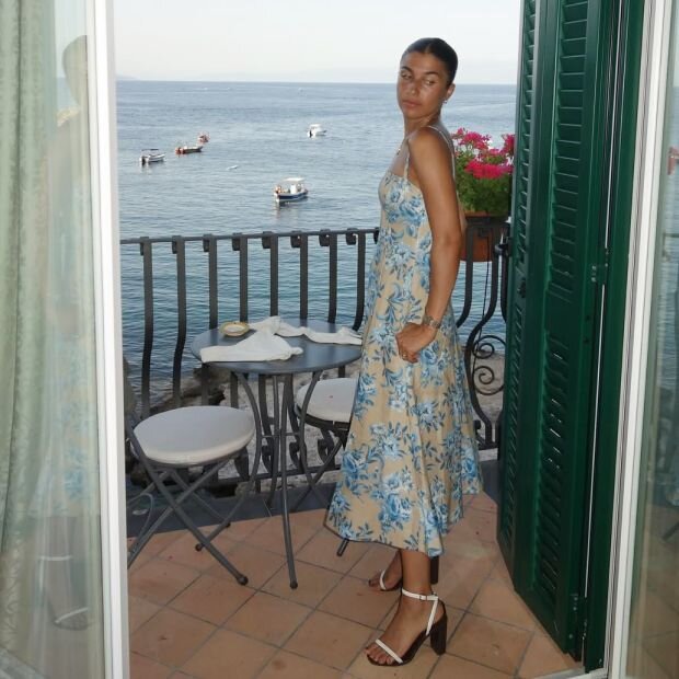 A model wearing white midi dress with a blue floral pattern. 