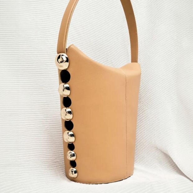 A beige leather bucket bag featuring metal stud embellishments down the sides.