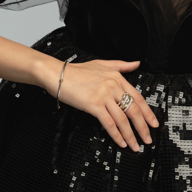 A model wearing a diamond 
gold two-tone ring comprised of 4 rings with orbiting annulet connectors create a linked design.