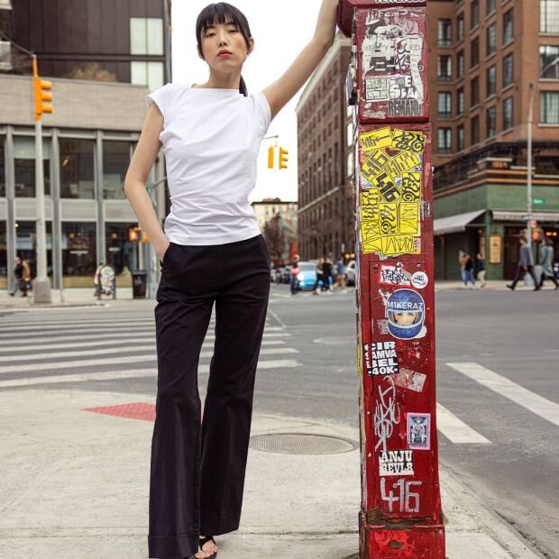 A model wearing a white cap sleeve tee with an asymmetric neckline, paired with black wide lef jeans with thick cuffs at the ankle.