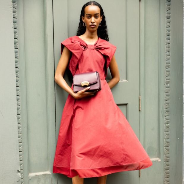 A model wearing a red midi dress with a classic A-line shape and cape-like puff sleeves that mimic a bow across the chest.
