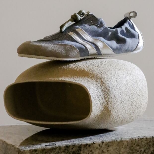 A blue denim sneaker with a corded zipper pull, suede toe cap, and contrasting white side stripes.