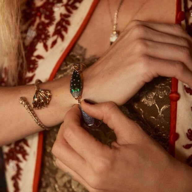 A model wearing a scarab gold silver multi-stone bracelet layered with a gold diamond bracelet with a mermaid splash.