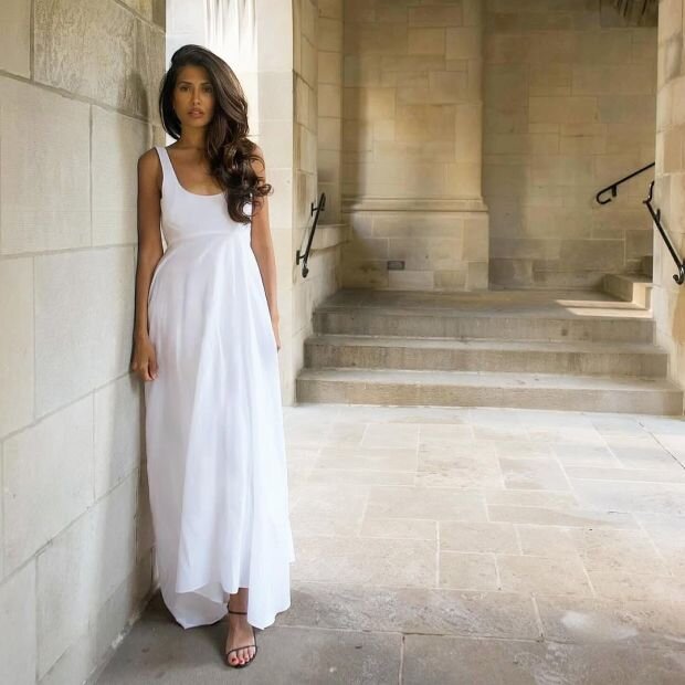 A woman wearing a sleeveless white maxi dress featuring an empire waist.