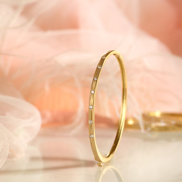 An 18k gold hinged bangle decorated with a linear array of seven ethically sourced diamonds.