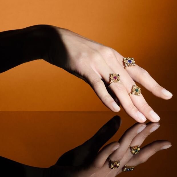 A model's hand wearing 3 large stamp gold peridot and diamond ring in green, pink, and blue.