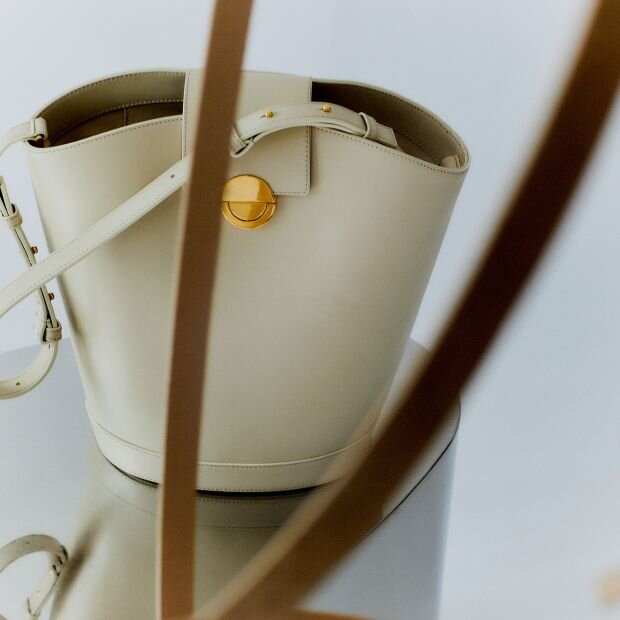 A white leather bucket bag featuring polished gold-tone hardware and a push-lock closure.