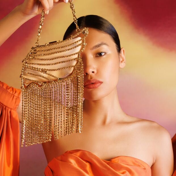 A model holding a gold leather bag with crystal embellishments and dimensional fringe trim.