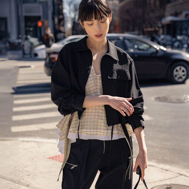 A model wearing a black cropped woven wool-blend shirt jacket with a plaid-print silk organza peplum top underneath.