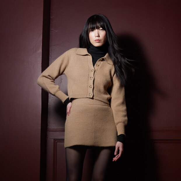 A model wearing a beige wool structured button up cardigan with collars, and a matching wool skirt.