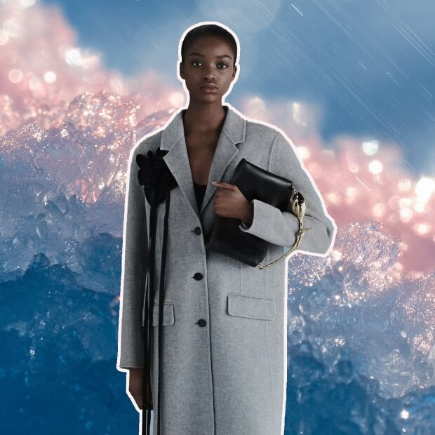 A model wearing a grey single-breasted tailored coat with a silk black ribbon appliqué.