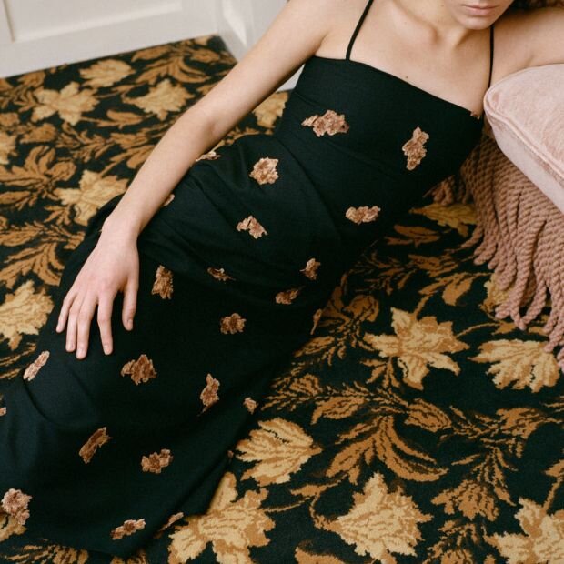 A women wearing a midi dress with a floral pattern and a gathered pleat at the waist, featuring an asymmetric hem.