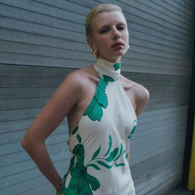 A woman wearing a cream and green floral printed halter neck dress.