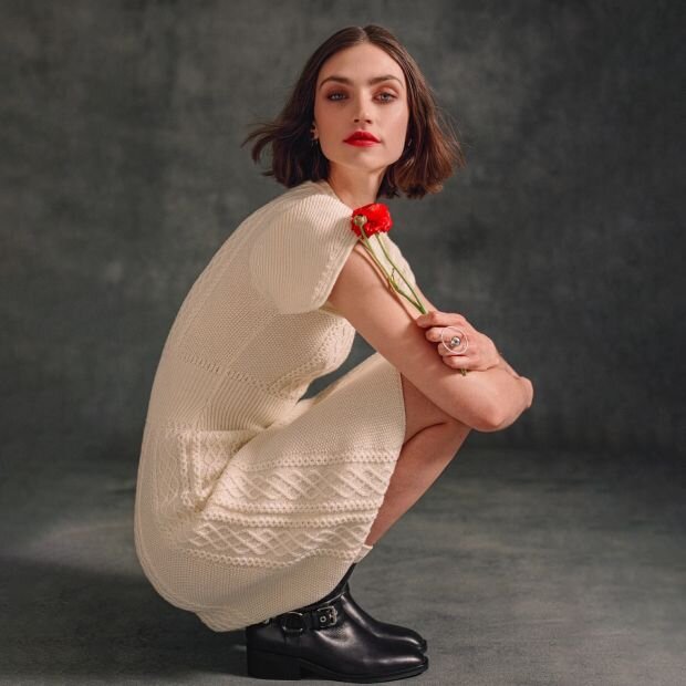 A model wearing a cream knitted sweater dress paired with black campus ankle boots.