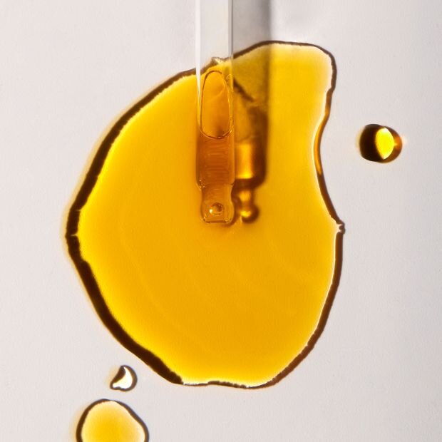 A glass dropper spilling an amber-colored serum on a white surface.