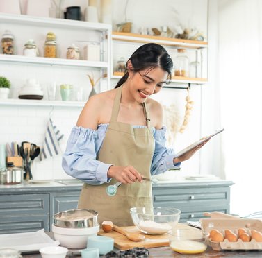 woman smiling while baking in the kitchen and holding a cookbook