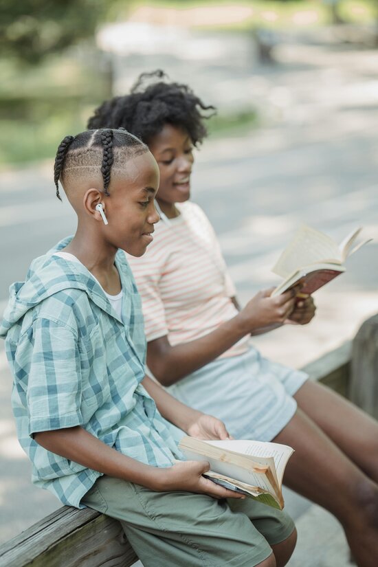 2 kids sitting outside reading books