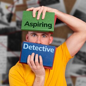 Man holding 2 books entitled Aspiring Detective