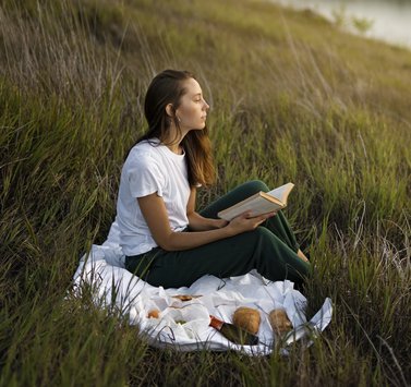 woman sitting on a blanket in the grass watching a sunset while reading a book