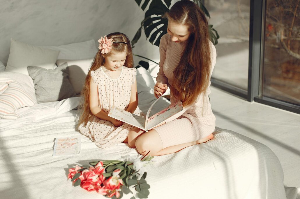 Mother and child sitting on a bed, reading a book.