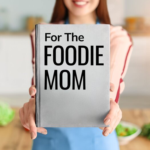 Woman holding up book in front of face that says: "For the Foodie Mom"