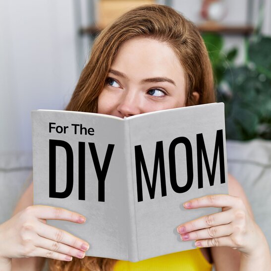 Woman holding up book in front of face that says: "For the DIY Mom"