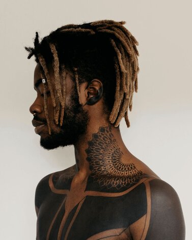 Man with dreadlocks and black work tattoos on his neck and chest