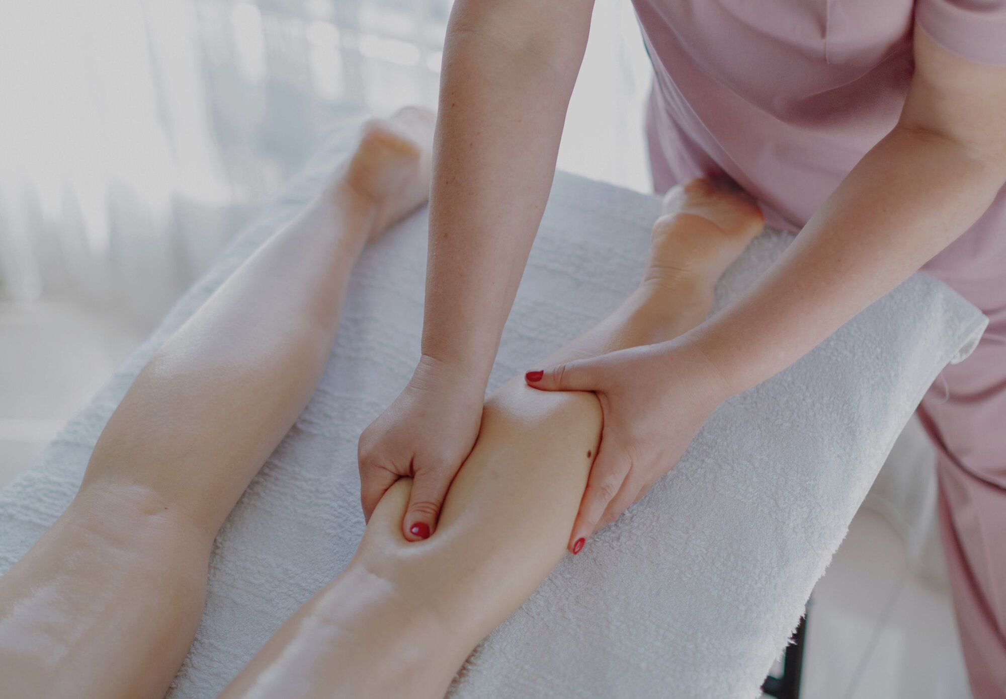 Eine Frau behandelt mit Lymphdrainage an den Waden einer Patientin
