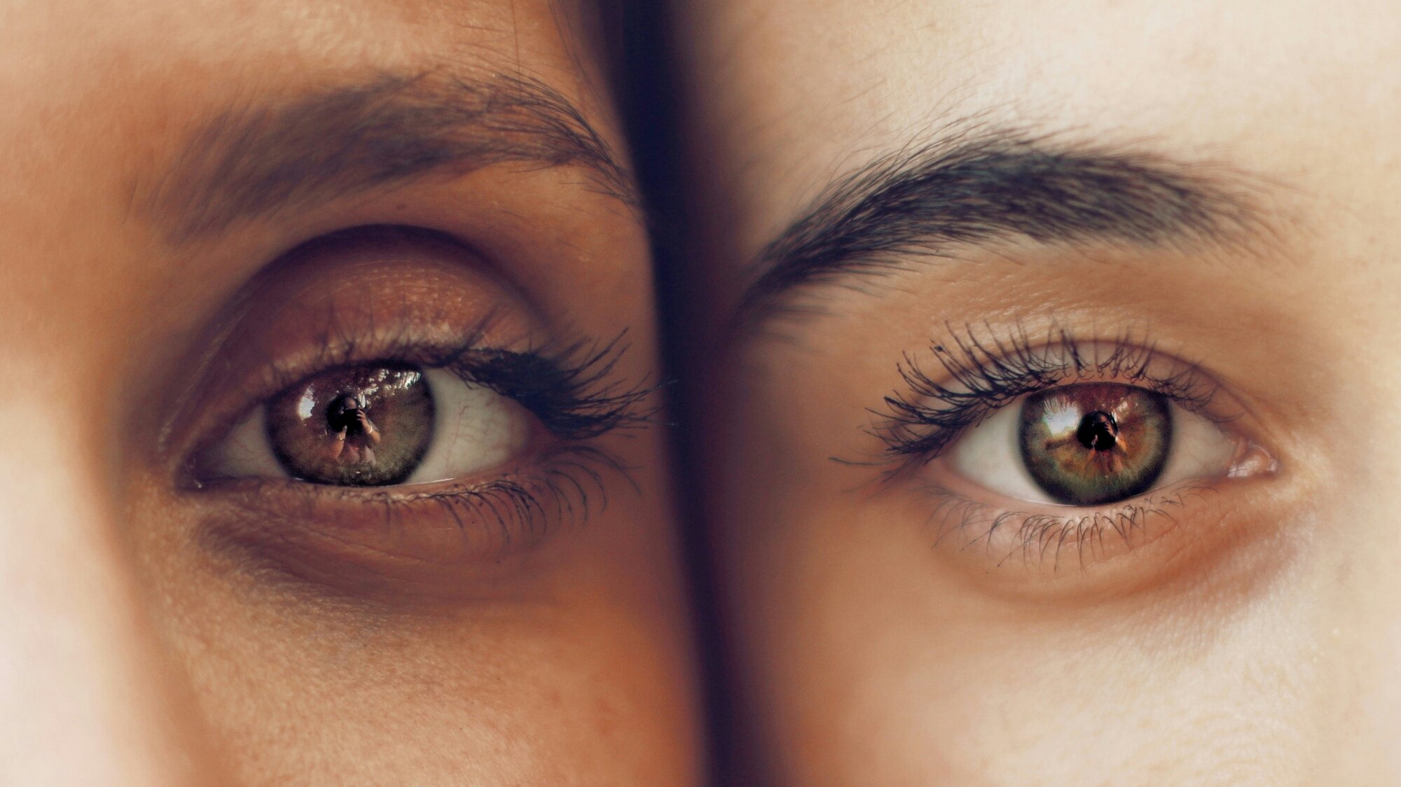 Zwei Menschen schauen Wange an Wange gerade nach vorne. Im Fokus des Fotos sind die Augen der beiden.