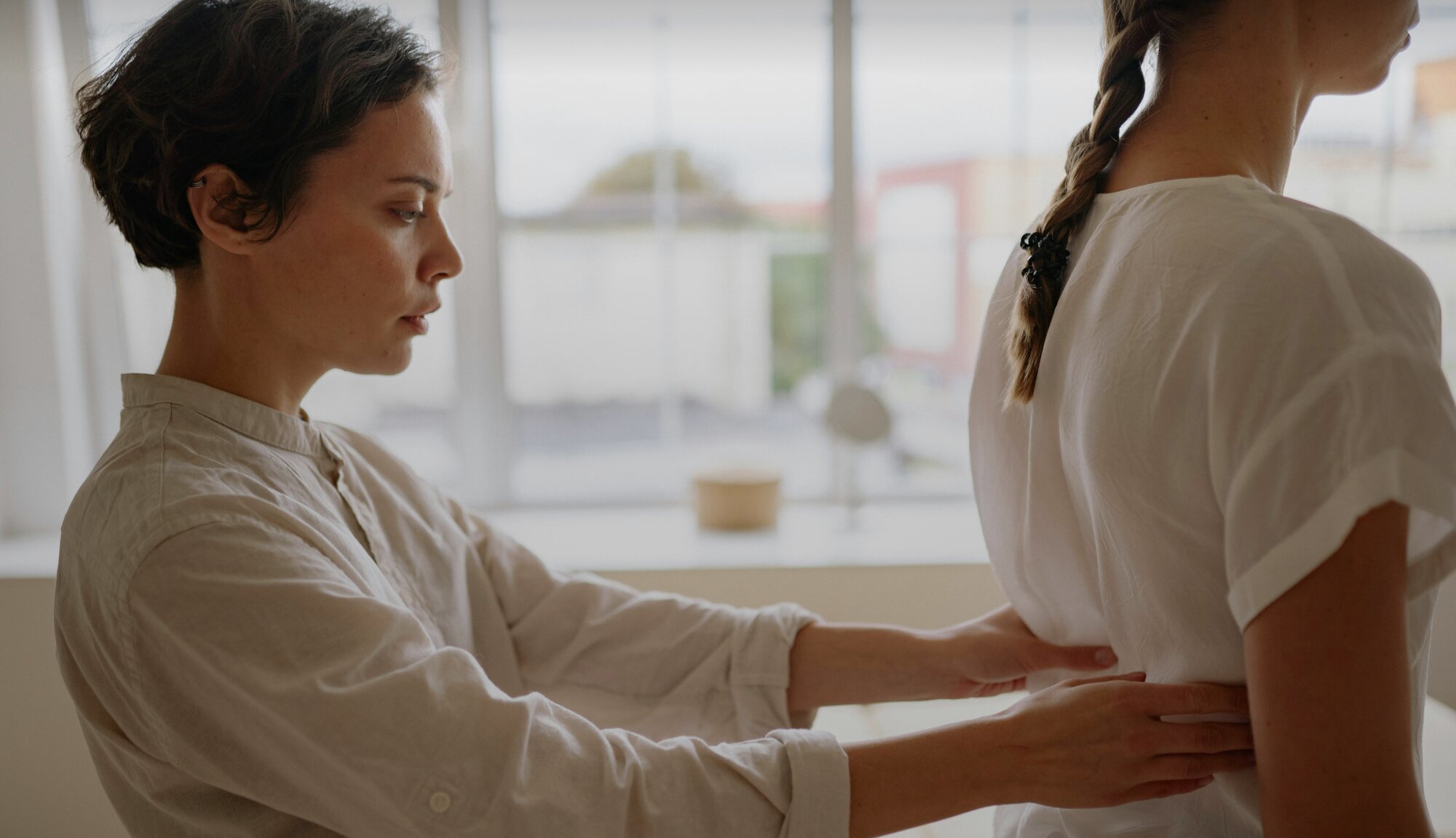 Osteopathie Behandlung in der Praxis: Die Osteopathin begutachtet den Rücken einer Patientin.