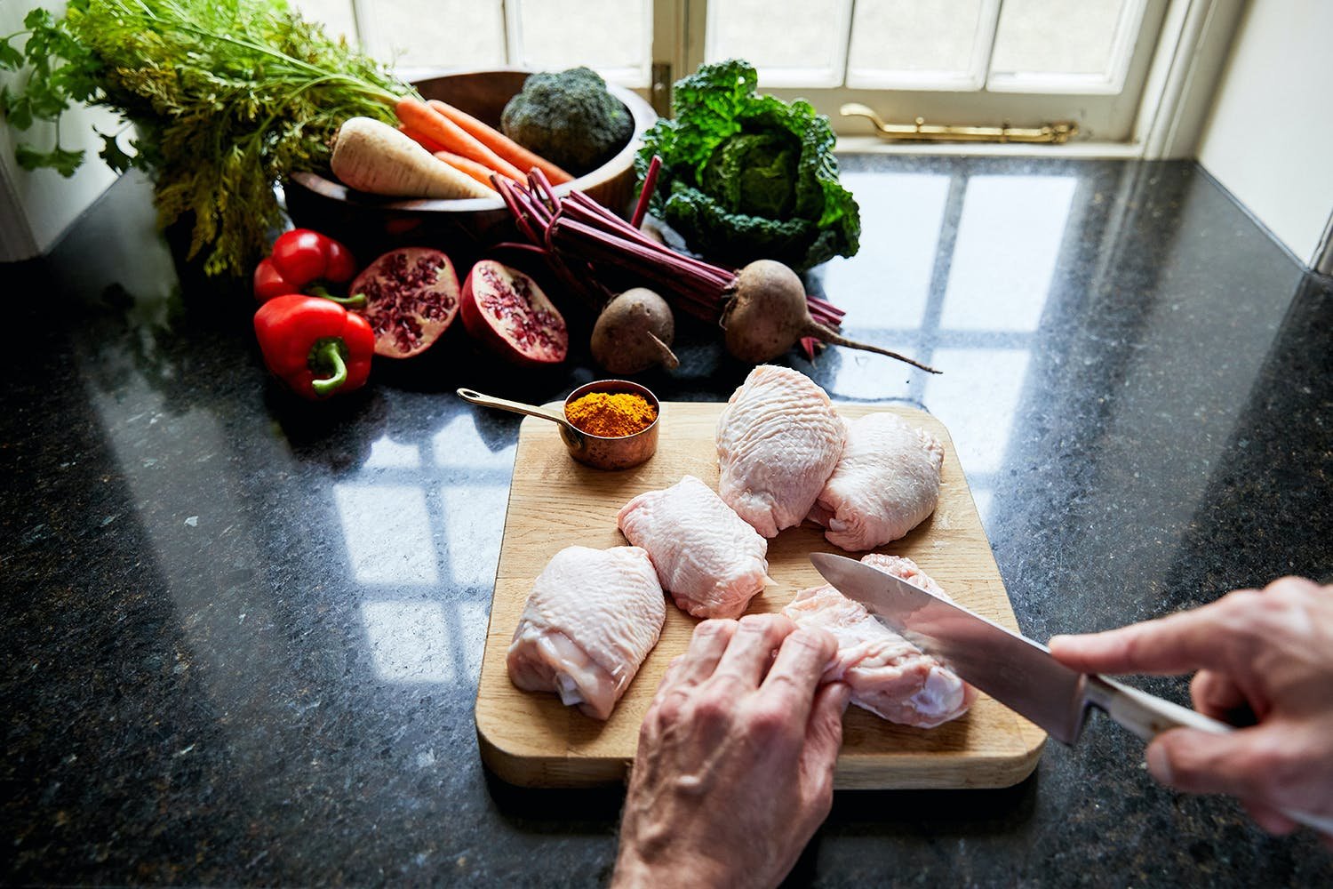 someone cutting raw chicken on a chopping board