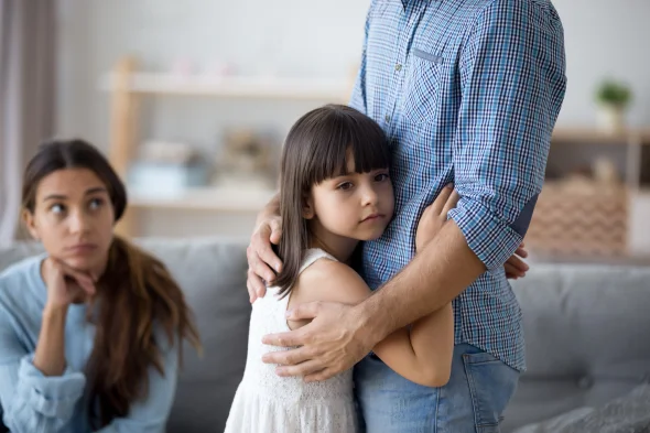 A child hugging her father while her mother is watching 