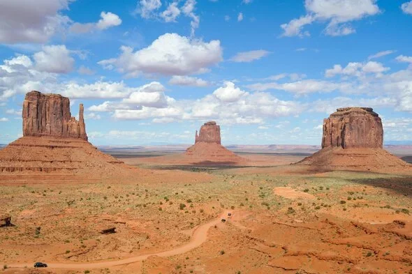 Monument Valley's iconic sandstone buttes under a bright blue sky, representing the unique landscapes of Arizona, with a road winding through the desert.