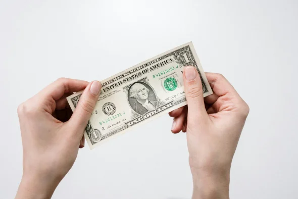 Hands holding a U.S. one-dollar bill against a white background.