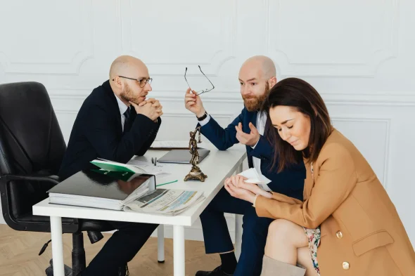 A couple in a tense discussion with a lawyer at a desk.