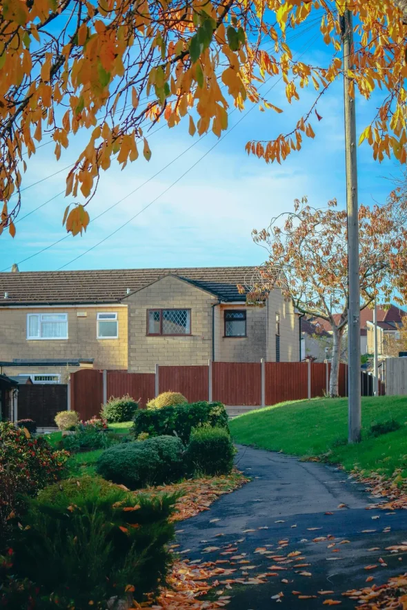 A suburban home with a garden path, autumn leaves, and blue sky.