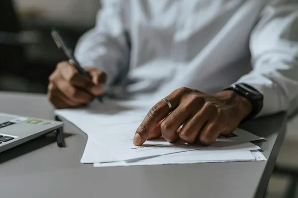 Close-up of a person reviewing and signing documents, symbolizing legal paperwork, contracts, or agreements often involved in divorce proceedings.