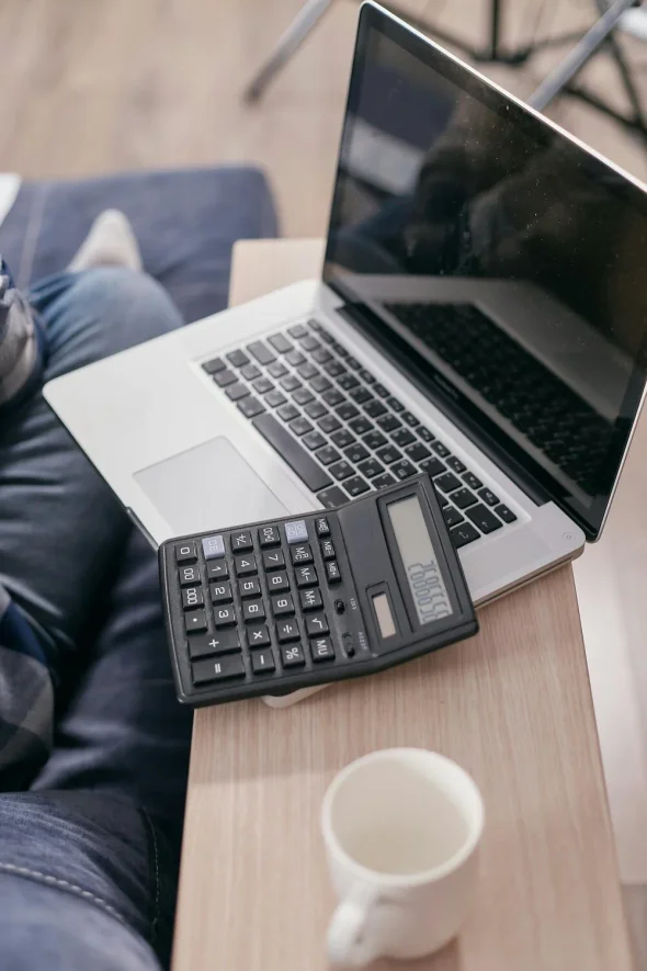 A laptop, calculator, and a coffee mug on a wooden table.