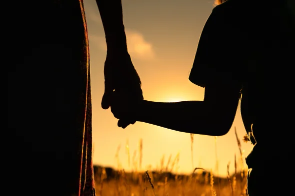 A parent and a child holding hands during sunset