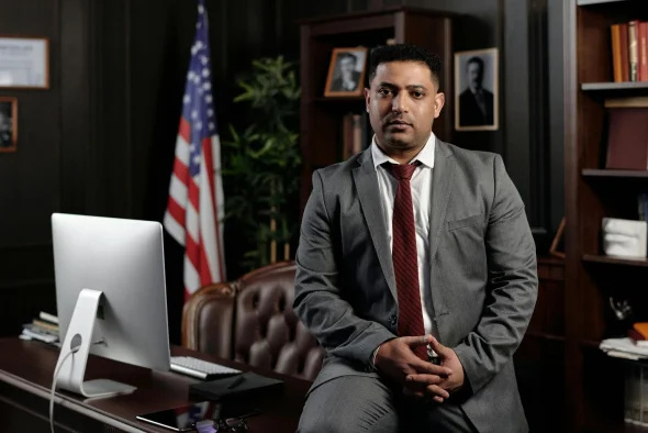 An attorney in a suit sitting in an office with an American flag.