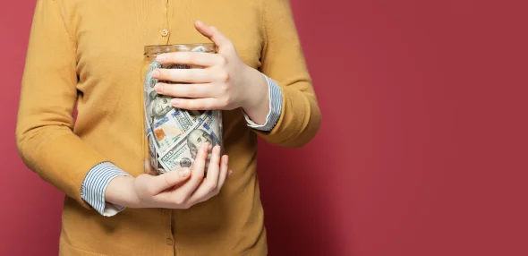 A woman holding a jar full of USD to her chest 