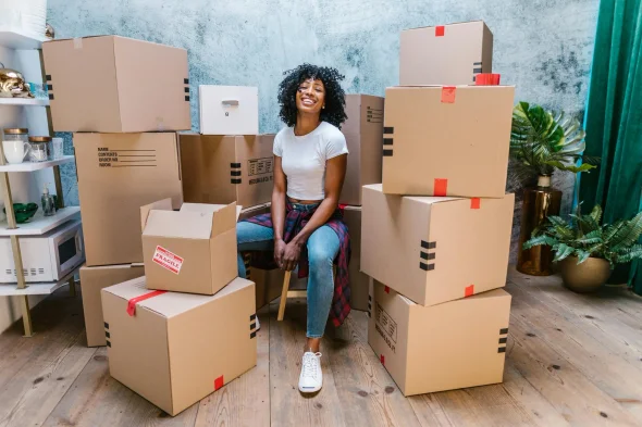 A woman sitting amidst stacked moving boxes, symbolizing relocation or life changes.