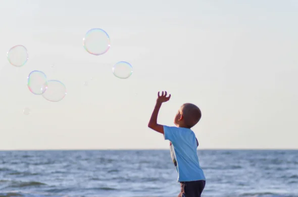 A child playing with bubbles by the sea under a clear sky.