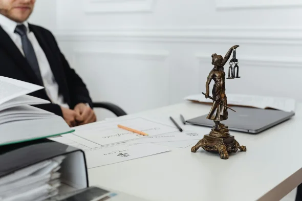 A desk with legal documents, a Lady Justice statue, and a lawyer seated.