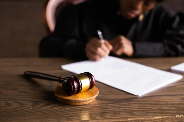 A gavel on a wooden table with a family court judge writing in the background.