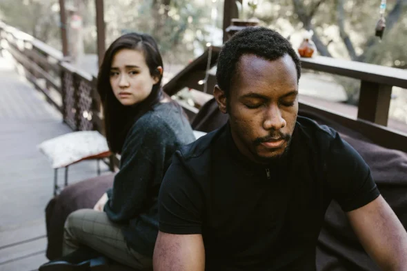 A couple sitting apart on a wooden porch, both appearing emotionally distant, symbolizing relationship struggles, such as divorce or separation.