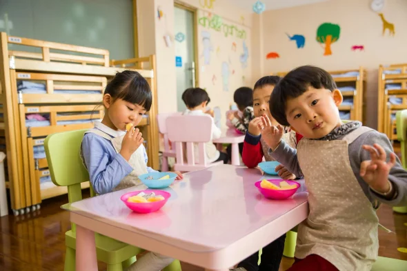 Children eating snacks at a colorful table in a daycare classroom.