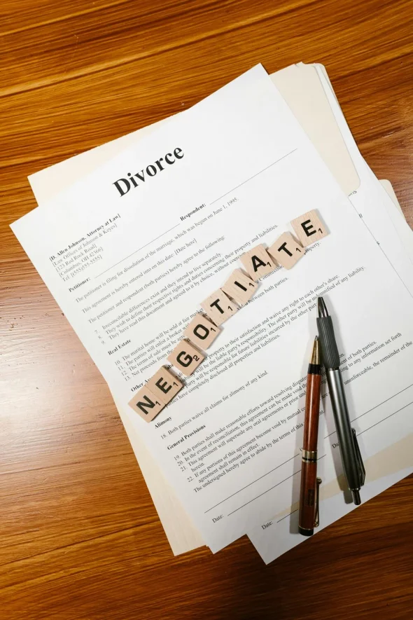 A divorce document on a desk with pens and "NEGOITATE" spelled in tiles.