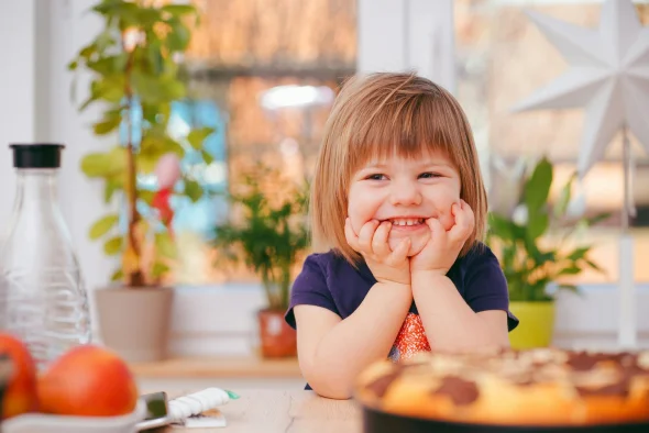 Smiling child at a table in a sunlit room with colorful decor.